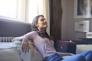 woman-in-pink-long-sleeve-shirt-and-blue-denim-jeans-sitting-on-brown-sofa-with-her-eyes-closed